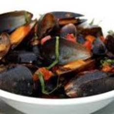 A bowl of mussels with sauce and herbs.